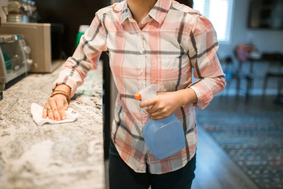 A woman is carefully wrapping a sofa in protective material while packing boxes in a bright room.